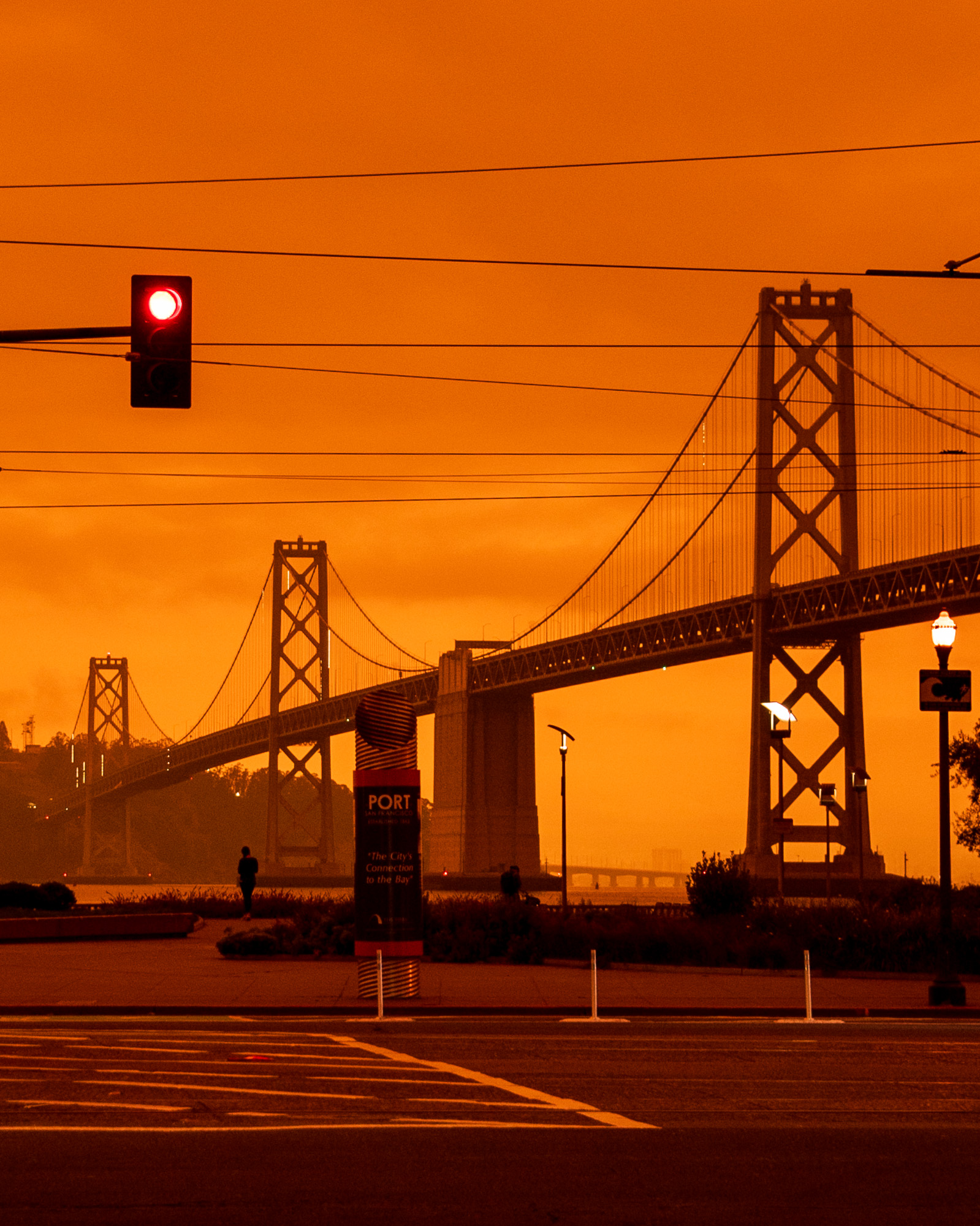 Bay Bridge and red traffic light under orange sky